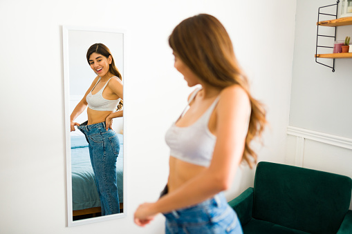 Excited smiling young woman losing weight and wearing jeans too big for her while feeling satisfied with the results of her diet